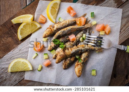 deep fried sardines with lemon and salad on white paper