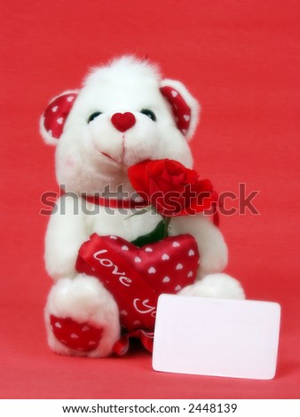 Teddy bear with red valentine heart on red background with blank card and little blur