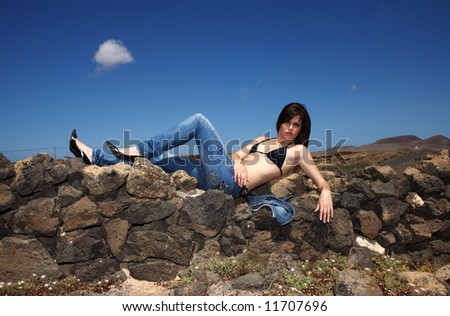 sexy young woman with blue jeans over stones under blue sky