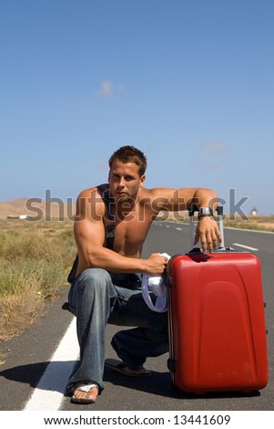 young athletics man in the middle of a road with red suitcase