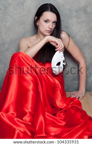 Elegant caucasian woman in red silk sitting on the floor with a face mask