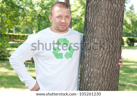 Man with recycle logo on his shirt embracing tree trunk in a green park