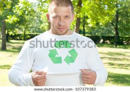 Positive caucasian ecologist demonstrating recycling logo on his shirt and looking at camera