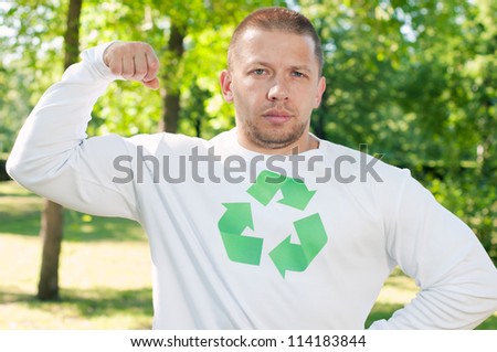 Outdoor portrait of a strongman flexing his muscles and wearing a shirt with green recycling symbol