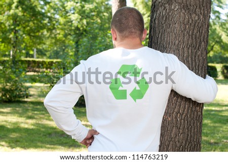 Ecologist with recycle logo on his shirt embracing a tree in a green park: eco friendly lifestyle concept