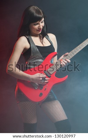 Vertical shot of a young woman playing the electric guitar, dark background
