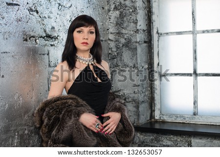 Elegant woman in black dress and fur coat standing by the window