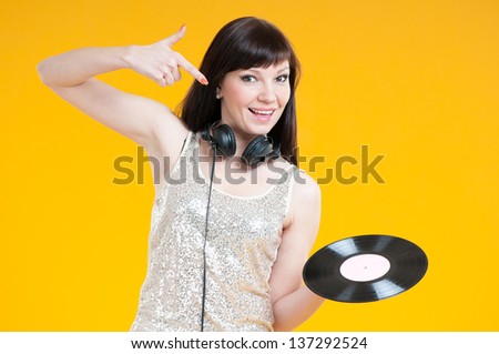Smiling and carefree young woman pointing at a vinyl record, yellow background, studio shot