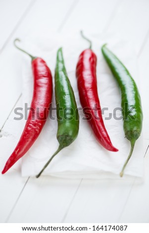 Red and green chili peppers over white wooden background