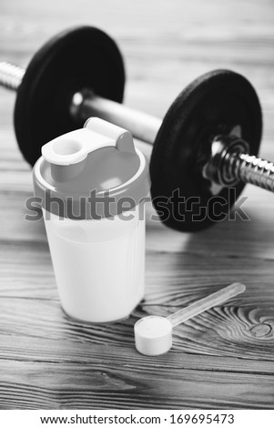 Protein drink, measuring scoop and a dumbbell, black and white shot