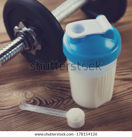 Protein shake with a measuring scoop and a dumbbell, close-up