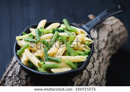 Frying pan with penne pasta and vegetables on wooden logs