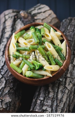 Penne with beans and broccoli on wooden logs, studio shot