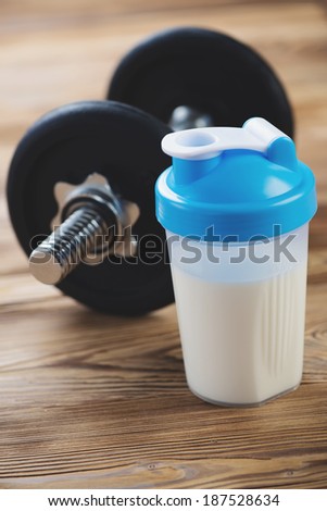 Protein shake with a dumbbell in the background, vertical shot