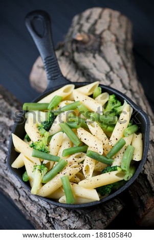 Penne pasta with vegetables in a frying pan on wooden logs