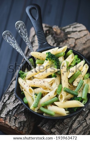 Penne with vegetables in a frying pan on wooden logs, close-up