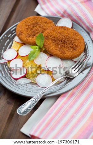 Glass plate with fried fish burgers, oranges and radish