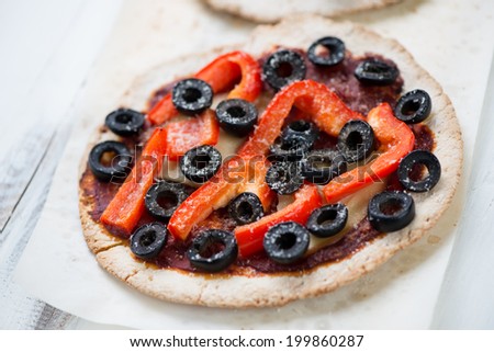 Mini pizza with red bell pepper and olives on a baking paper