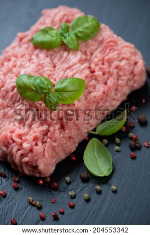Ground turkey meat with pepper and basil, black wooden surface