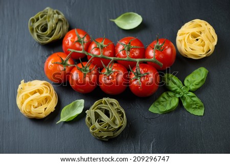 Branch of red tomatoes, colored tagliatelle and basil leaves