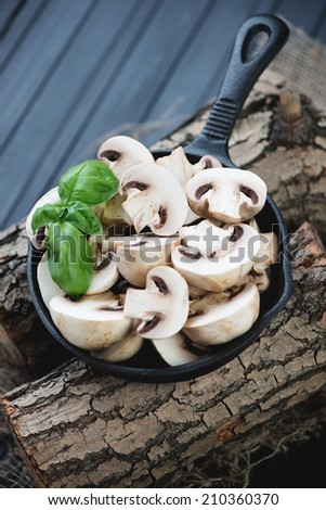 Frying pan with raw sliced champignons and basil on wooden logs