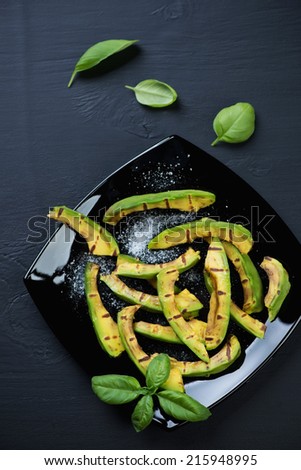 Grilled avocado with salt on a black glass plate, above view