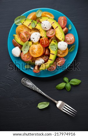 Vegetable salad with grilled avocado, black wooden surface