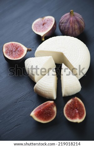 Sliced round cheese and fig fruits over black wooden background