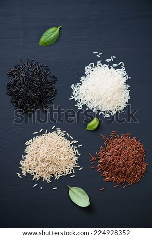 Red, brown, white and black rice over black wooden surface