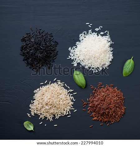 Red, brown, white and black rice over black wooden background