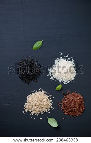 Red, brown, white and black rice over black wooden background