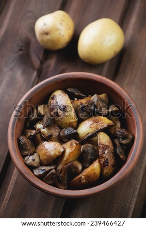 Ceramic bowl with roasted potato slices and mushrooms, close-up