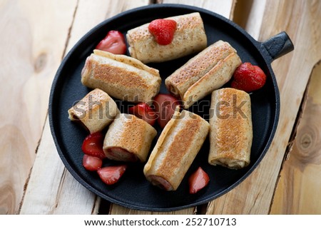 Frying pan with strawberry stuffed pancakes on wooden logs
