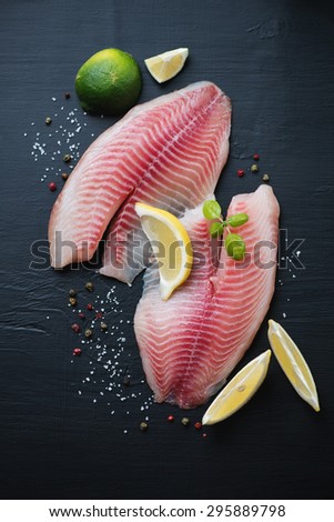 Raw tilapia filet with sea salt, pepper, lime and lemon, top view