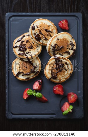 Pancakes served with chocolate and strawberries on a basalt dish, above view
