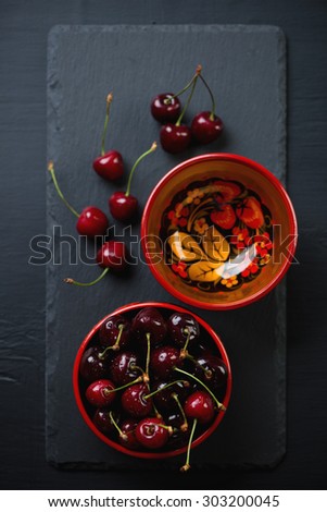Stone slate dish with sweet cherries in wooden bowls, above view