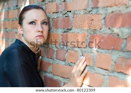 Serious young woman in black dress standing by a brick wall