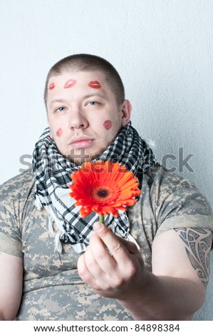 Portrait of tattoed caucasian man with lipstick marks on the face, holding Gerbera in his hands. Macho concept