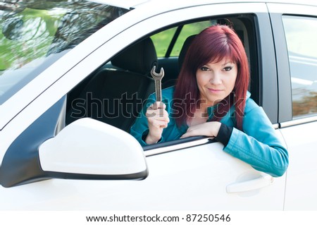 Portrait of a bewildered young woman sitting in a car outdoors with a wrench in her hand