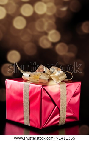 Red gift box with golden ribbon, glittery gold background
