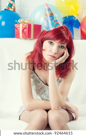 Party went wrong: sad caucasian woman in a party hat sitting on a sofa
