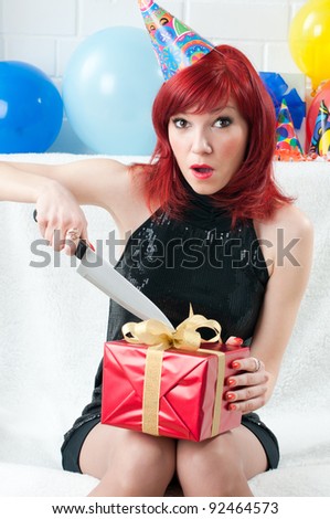 Surprised redheaded party woman opening a gift box with a kitchen knife
