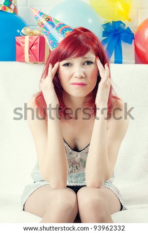 Stop the party: annoyed redheaded party girl with a headache sitting on a sofa