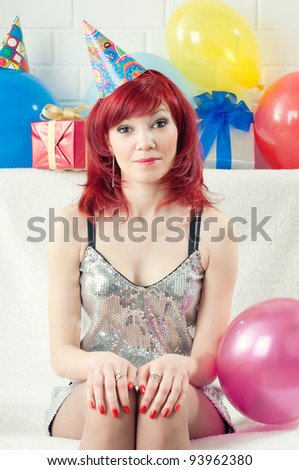 Smiling red-haired party woman in a party hat sitting on a sofa