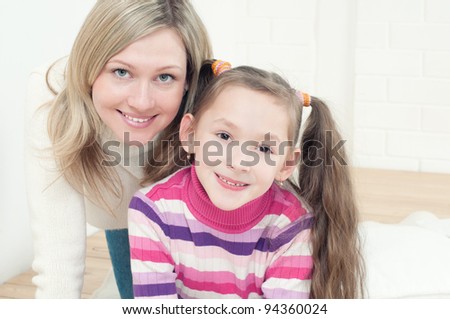 Happy mom and her daughter playing on the floor and looking at camera