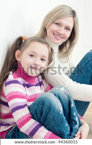Smiling little girl and her mom sitting on the floor at home and looking at camera