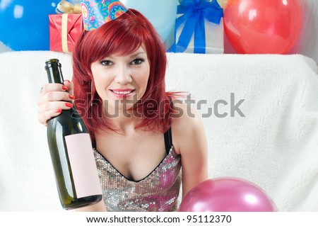 Smiling party girl sitting on a sofa with bottle of wine