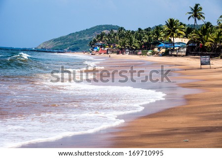 Exiting Anjuna beach panorama on low tide with white wet sand and green coconut palms, Goa, India
