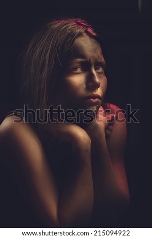 Dirty frightened teenage girl sits locked in a dark room