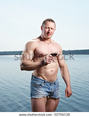 Muscular man with glass of red drink at  lake on sunny day